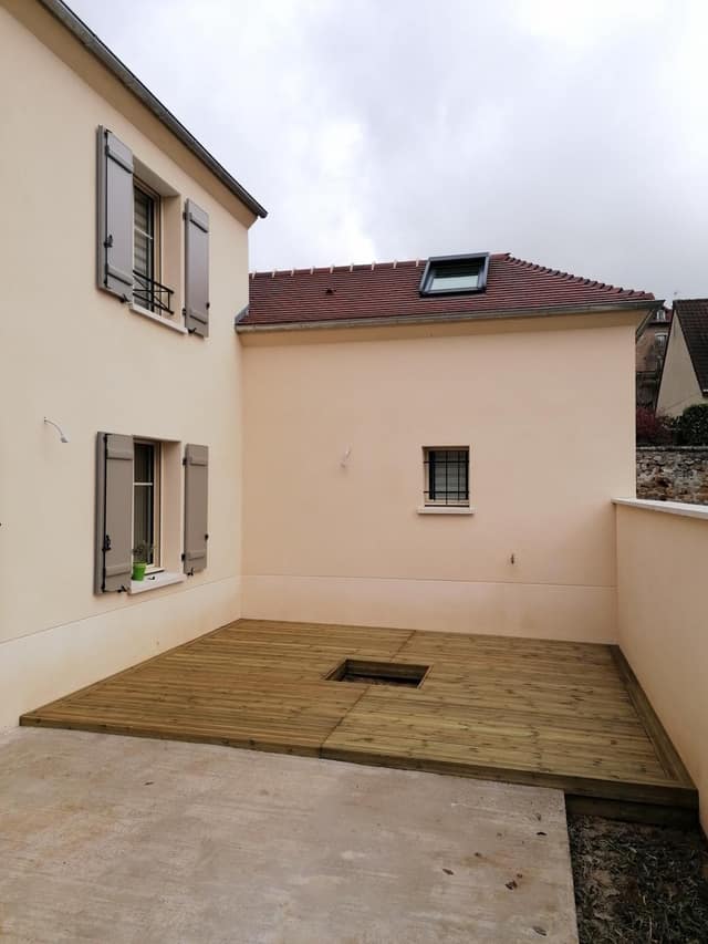 Terrasse en bois neuve posée dans une cour de maison avec réservation pour plantation