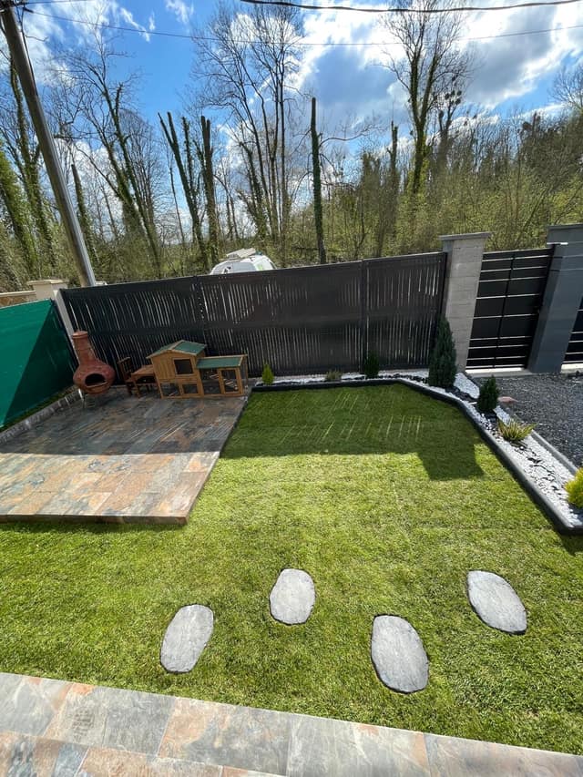 Jardin aménagé avec gazon, terrasse en dallage pierre, massifs et clôture occultante
