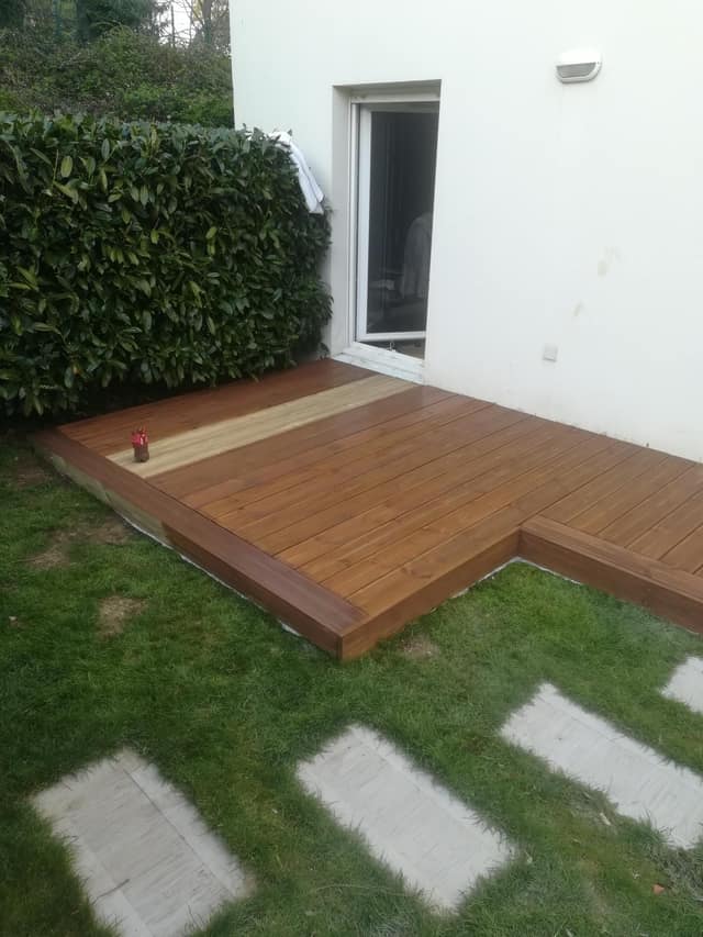 Terrasse en bois surélevée posée le long d'une maison avec pelouse et pas japonais