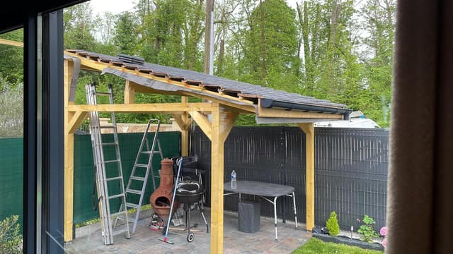 Abri de terrasse en bois avec toiture et gouttière posé le long d'une clôture