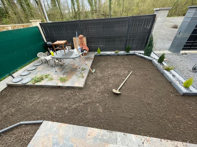 Préparation et nivellement de la terre avant pose de gazon dans un jardin clôturé
