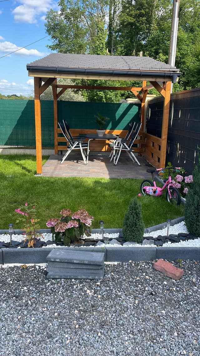 Pergola en bois terminée avec salon de jardin, gazon et massifs décoratifs en galets