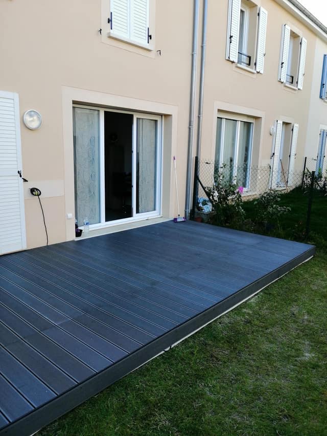 Terrasse en lames composite gris anthracite posée devant une baie vitrée avec pelouse